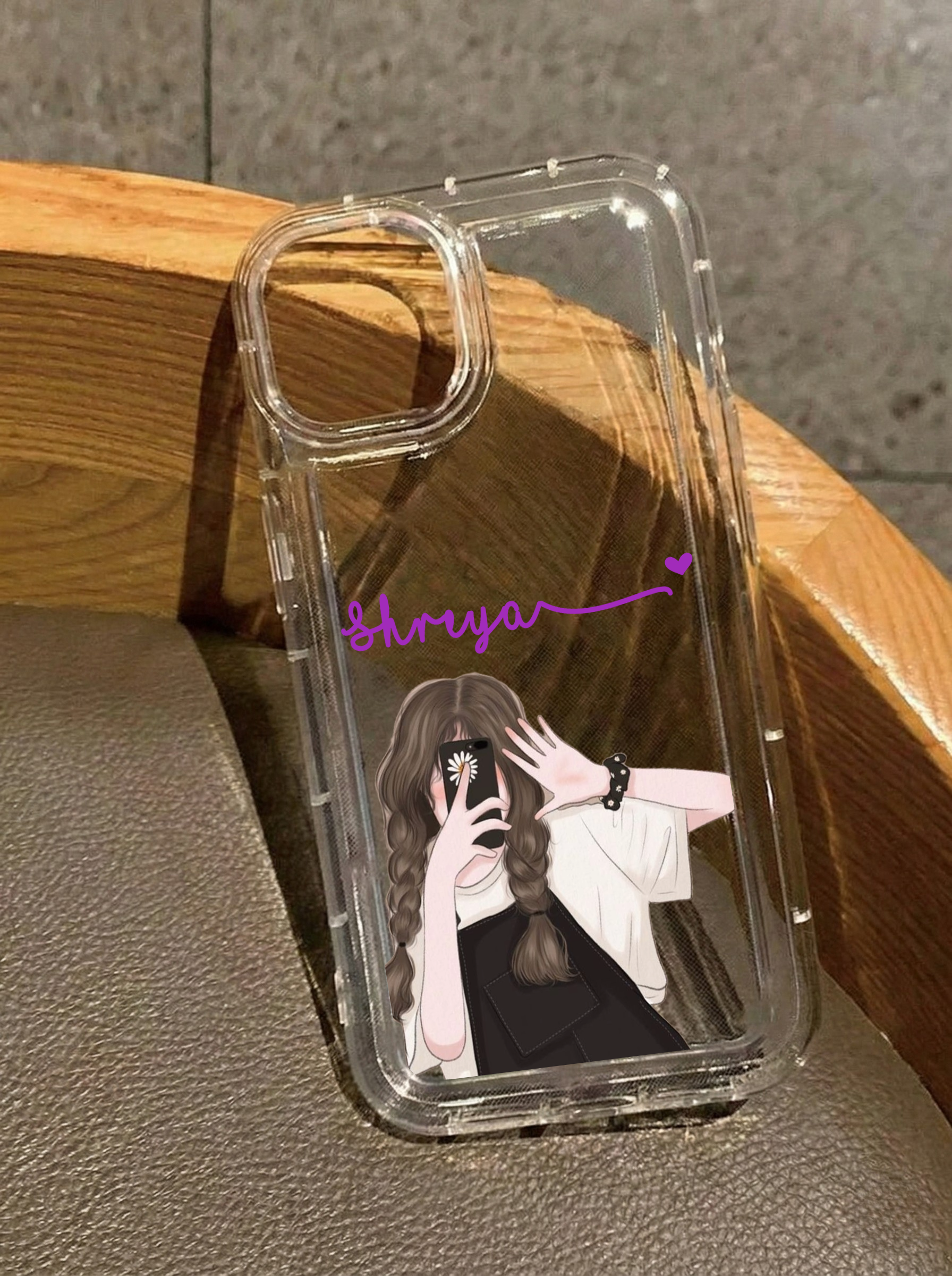 Clear iPhone 16 case featuring an illustration of a girl with braided hair in black overalls taking a selfie, customized with the name Shreya in purple text.